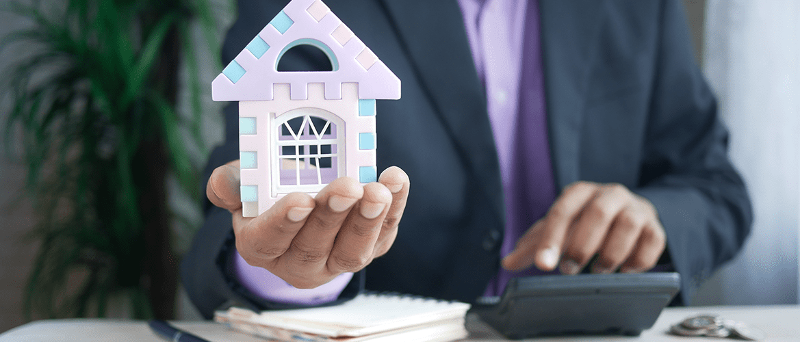 A man on a suit holding a house model explaining impound accounts