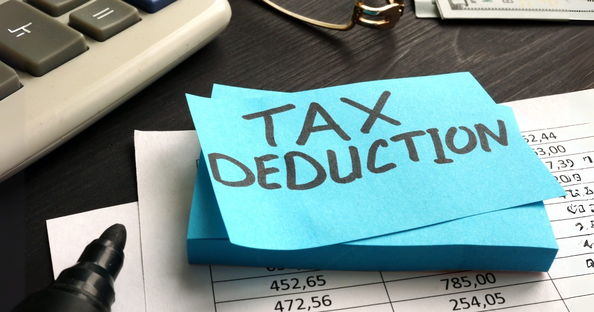 Sticky note with 'TAX DEDUCTION' written on it, placed on financial documents and next to a calculator and marker, symbolizing tax deductions for homeowners in 2025.